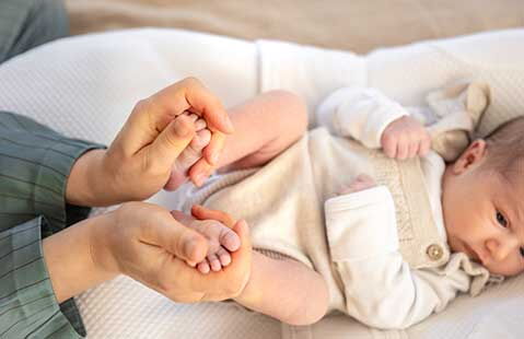 Mutter hält die Füße ihres Babys, massiert sanft die Fußsohlen, Säugling in beigem Stampler